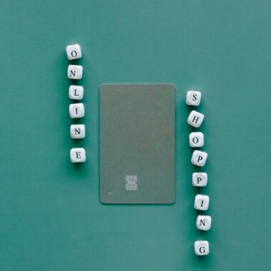 Flat lay with credit card surrounded by word "Online Shopping" on green backdrop.