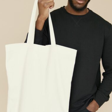 Portrait of a young man holding a blank white tote bag, ideal for mockup and branding purposes.